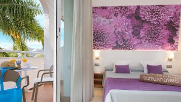 Habitación de hotel con balcón, cama con ropa de cama morada y un mural floral en la pared.