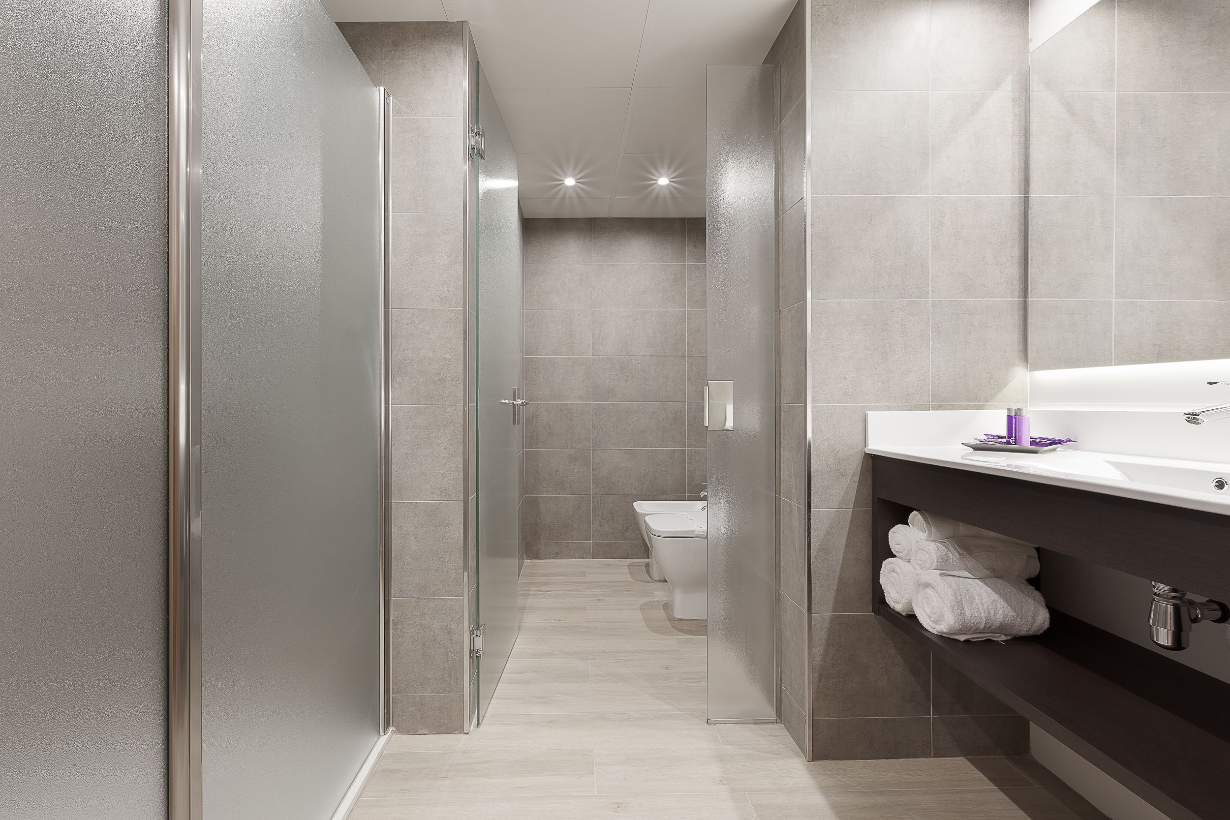Een moderne badkamer met een douchecabine van glas, een toilet en een wastafel met spiegel en handdoekhouder.