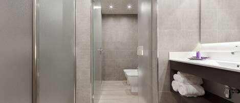 Een moderne badkamer met een douchecabine van glas, een toilet en een wastafel met spiegel en handdoekhouder.