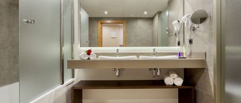 A modern bathroom with a large mirror, two sinks, a towel rack, and a shower area.