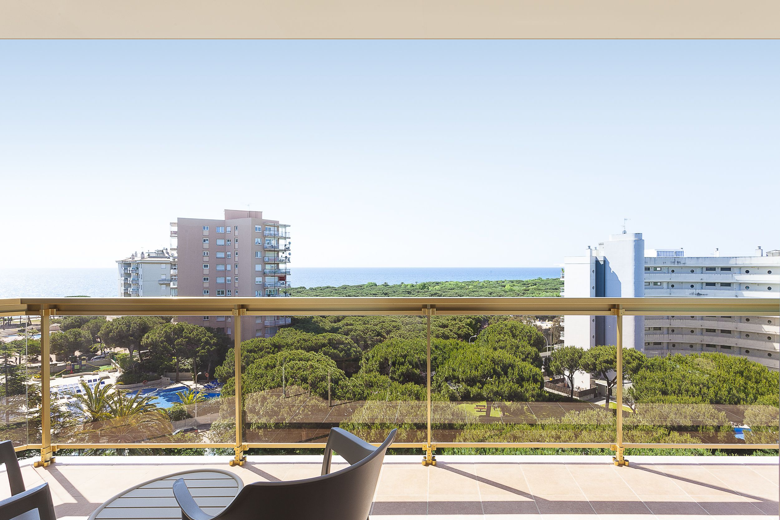Un balcon offrant une vue sur un paysage urbain, une étendue d’eau et un espace vert arboré.
