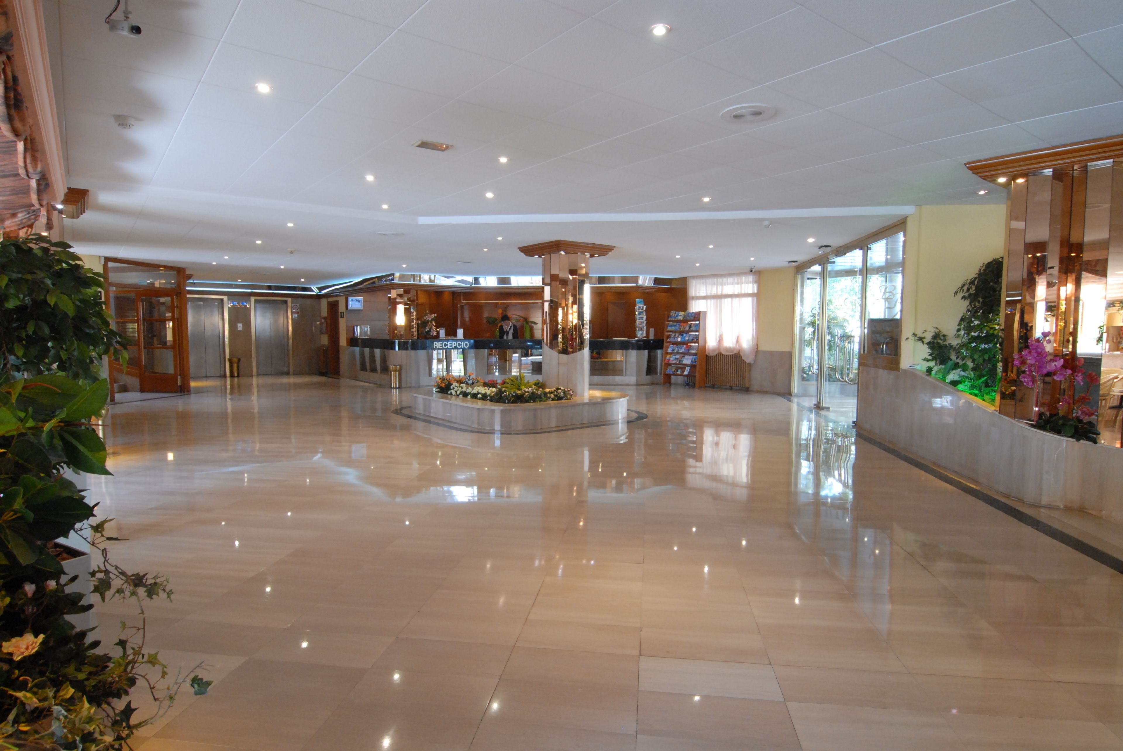 Un vestíbulo amplio con una mesa de recepción, ascensores y un arreglo floral central.