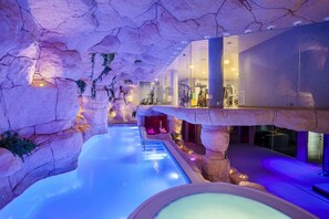 An indoor pool with a rocky cave-like ceiling, clear water, and a glass railing overlooking the pool. - Beverly Park Hotel & Spa (Blanes)