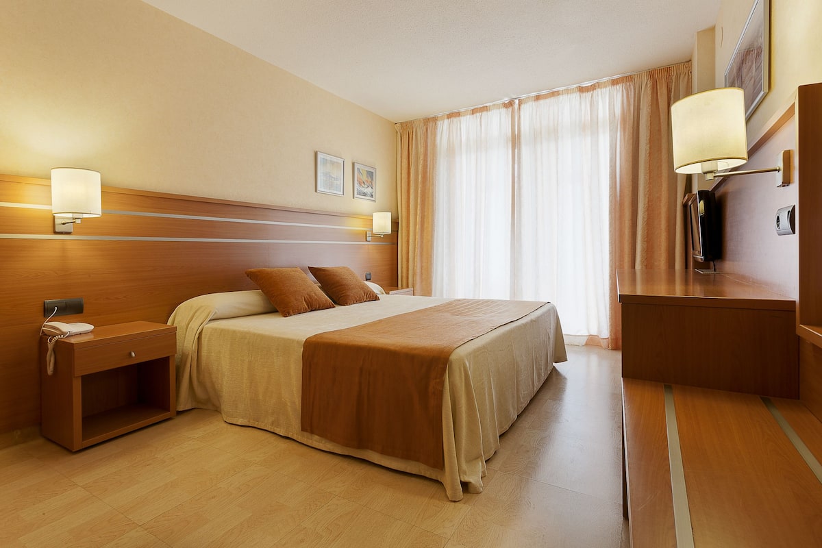 Una habitación de hotel con una cama grande, mesitas de noche, un escritorio y una lámpara.