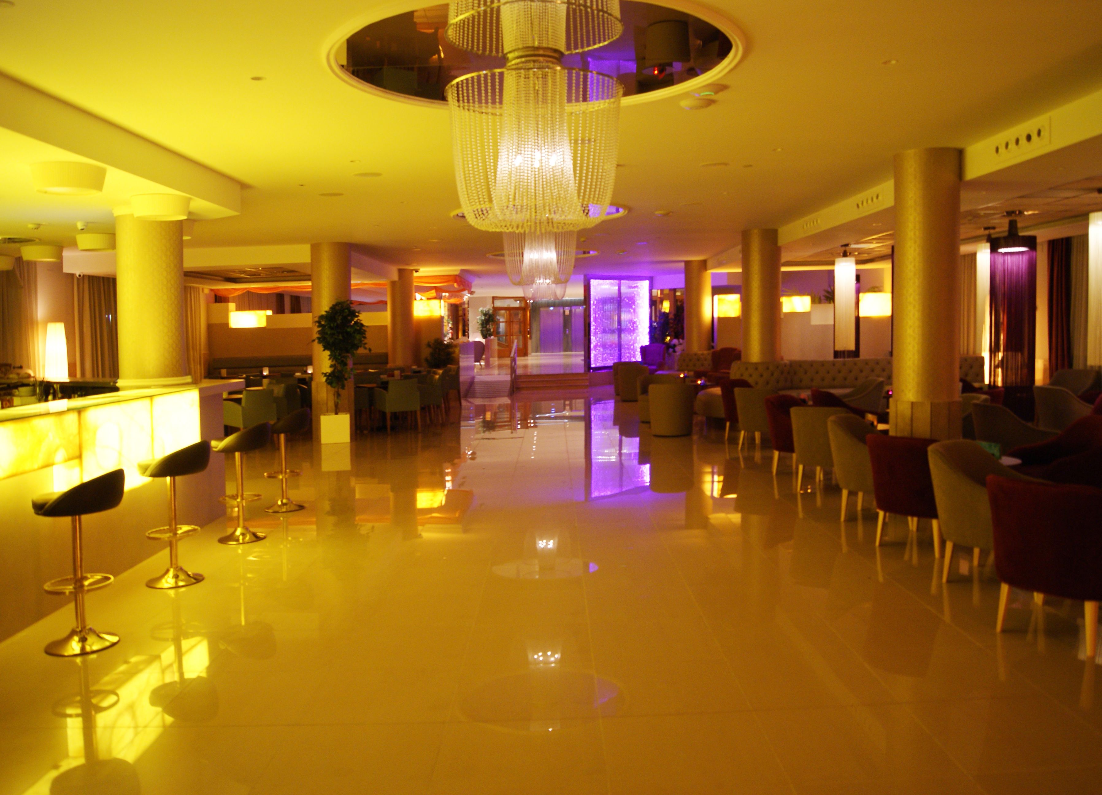 A spacious lobby with a reflective floor, a central chandelier, and seating areas.