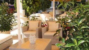 Un patio con mobiliario de mimbre, incluyendo sofás y una mesa, bajo un paraguas amarillo.