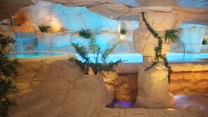 A spa area with a rock formation, a pool, and tropical plants. - Beverly Park Hotel & Spa (Blanes)