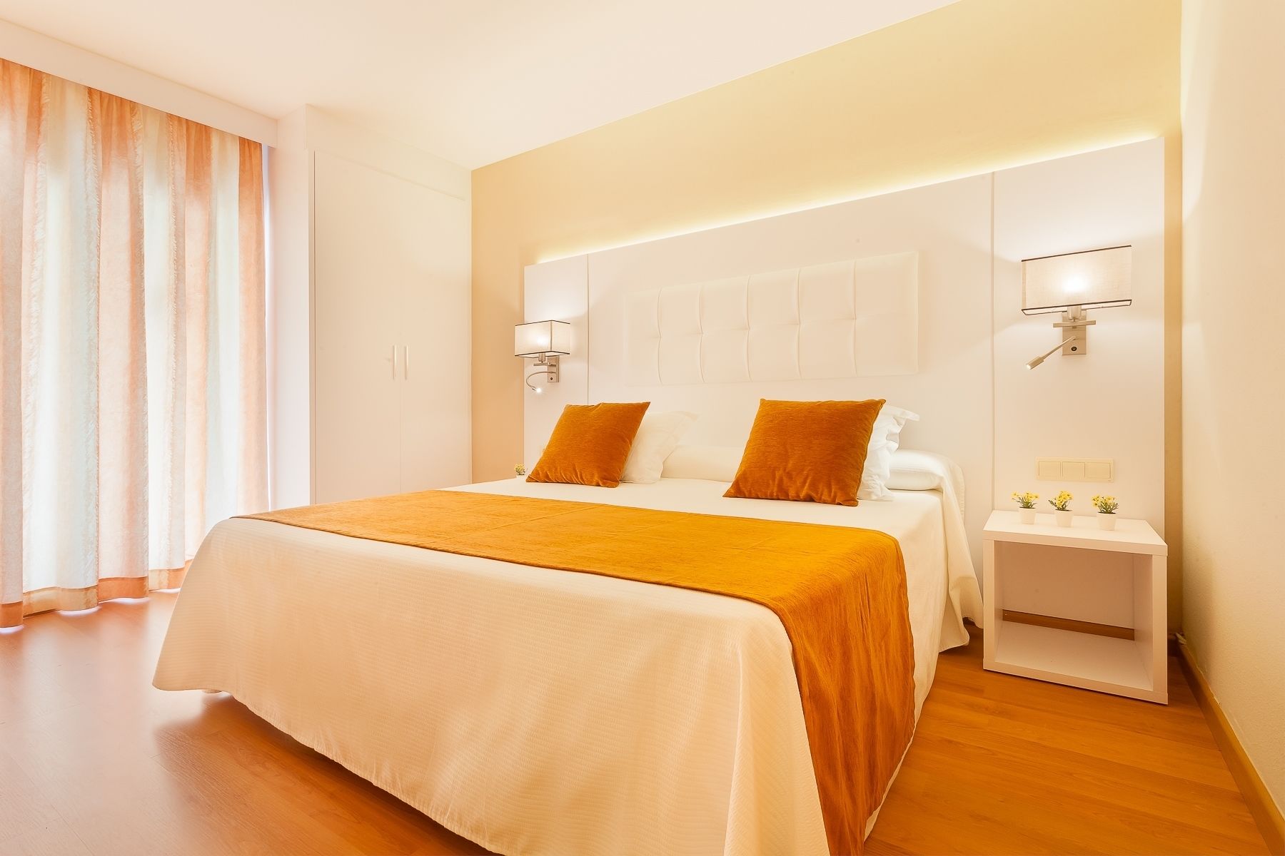 Een hotelkamer met een groot bed, twee bedlampen, een nachtkastje en een raam met gordijnen.