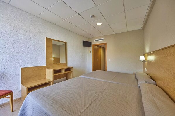 A hotel room with two beds, a wooden desk, a mirror, a television, and a door.
