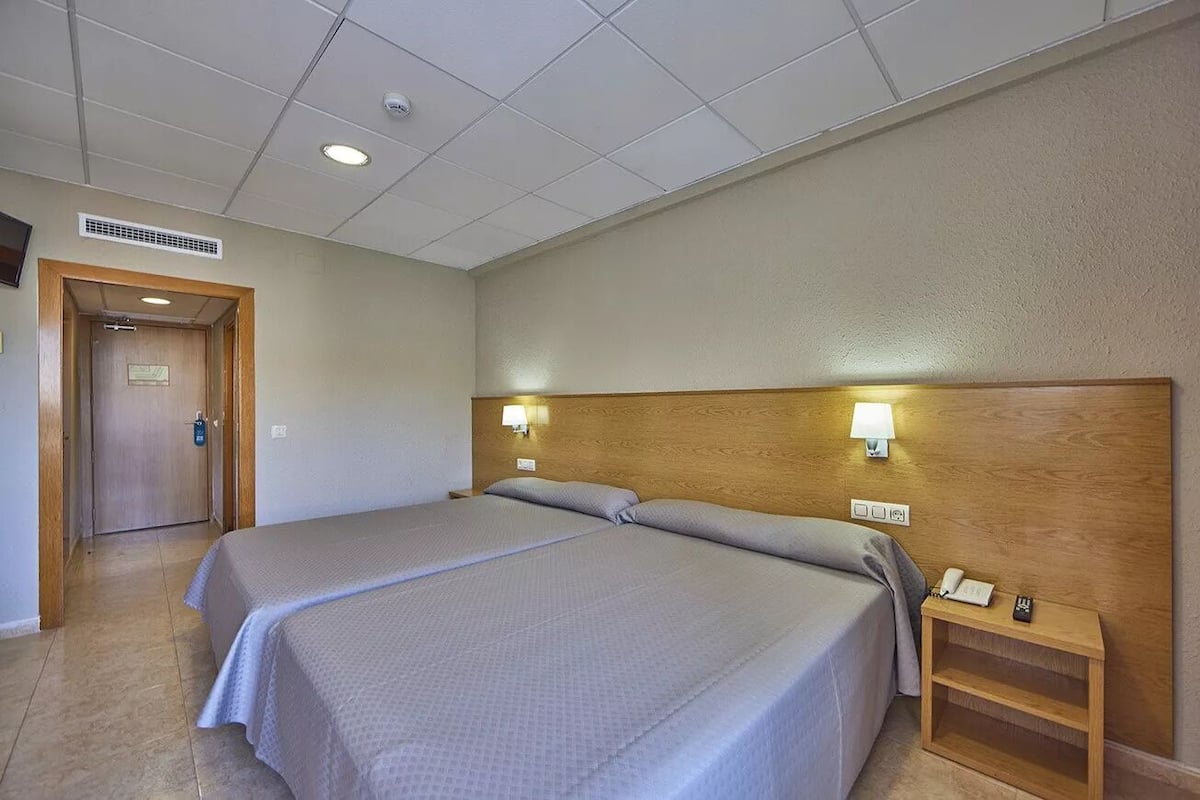 Une chambre d’hôtel avec deux lits, une tête de lit en bois, des lampes de chevet, une table de chevet avec un téléphone et une porte avec une serrure.