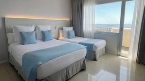 A hotel room with two beds, a view of the sea, and a balcony.