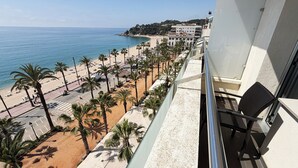 A balcony with a view of a beach, palm trees, and a building in the background.