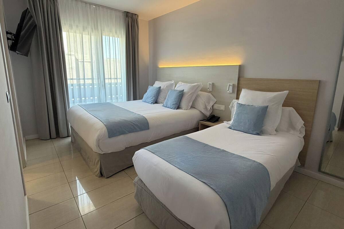 Habitación de hotel con dos camas, un televisor montado en la pared y una ventana con cortinas.