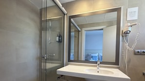 A modern bathroom with a glass-enclosed shower, a white sink, and a large mirror.