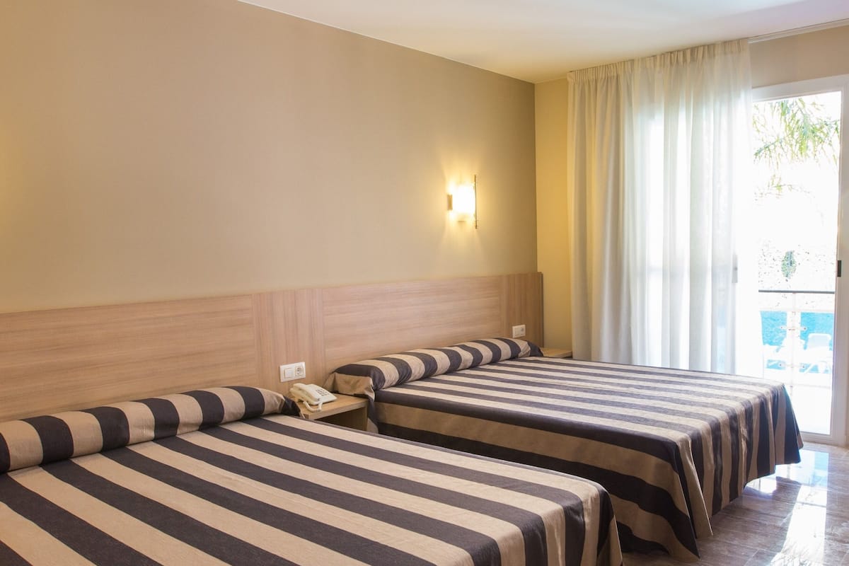 A hotel room with two beds, a bedside telephone, and a window with curtains.