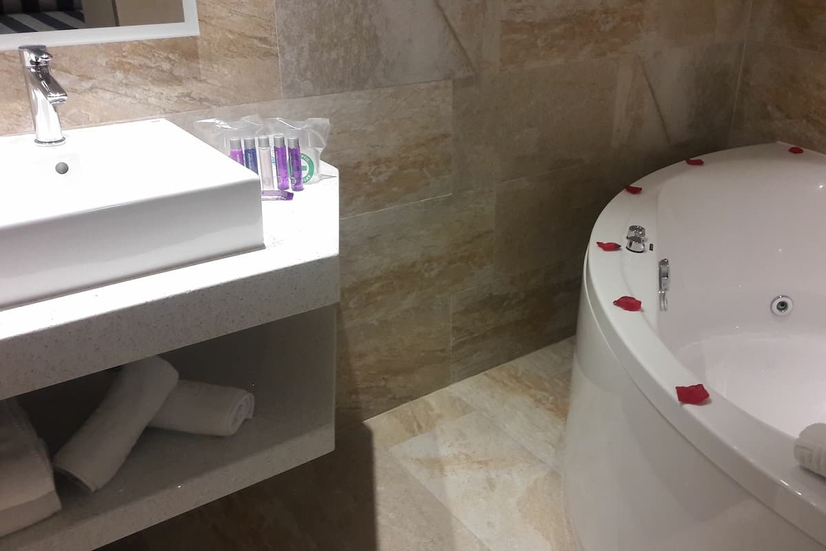 A bathroom with a white sink, toiletries, and a bathtub with rose petals.