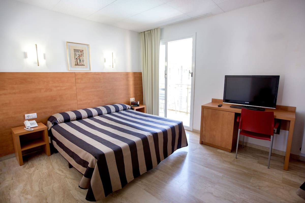 A hotel room with a large bed, a desk with a television, a chair, and a window with curtains.