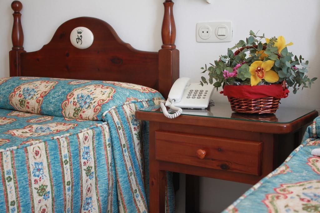 A bedroom with a wooden headboard, a bedside table with a telephone and a basket of flowers, and a bed with floral bedding.