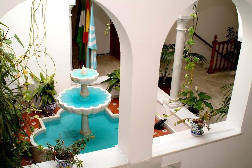A courtyard with a central fountain, surrounded by potted plants and white arches.