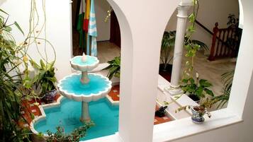 A courtyard with a central fountain, surrounded by potted plants and white arches.