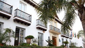 Un bâtiment blanc doté de balcons, un grand pot de fleurs et une enseigne indiquant « Hôtel ».