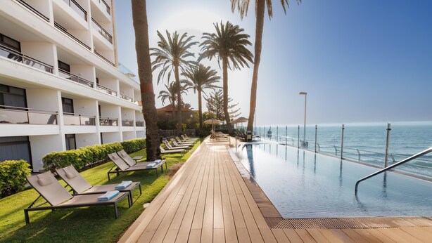 A poolside area with lounge chairs, a wooden deck, and a view of the ocean. - Don Gregory by Dunas, Adults Only (San Bartolomé de Tirajana)