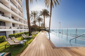 Un área junto a la piscina con sillones de descanso, una terraza de madera y vistas al océano.
