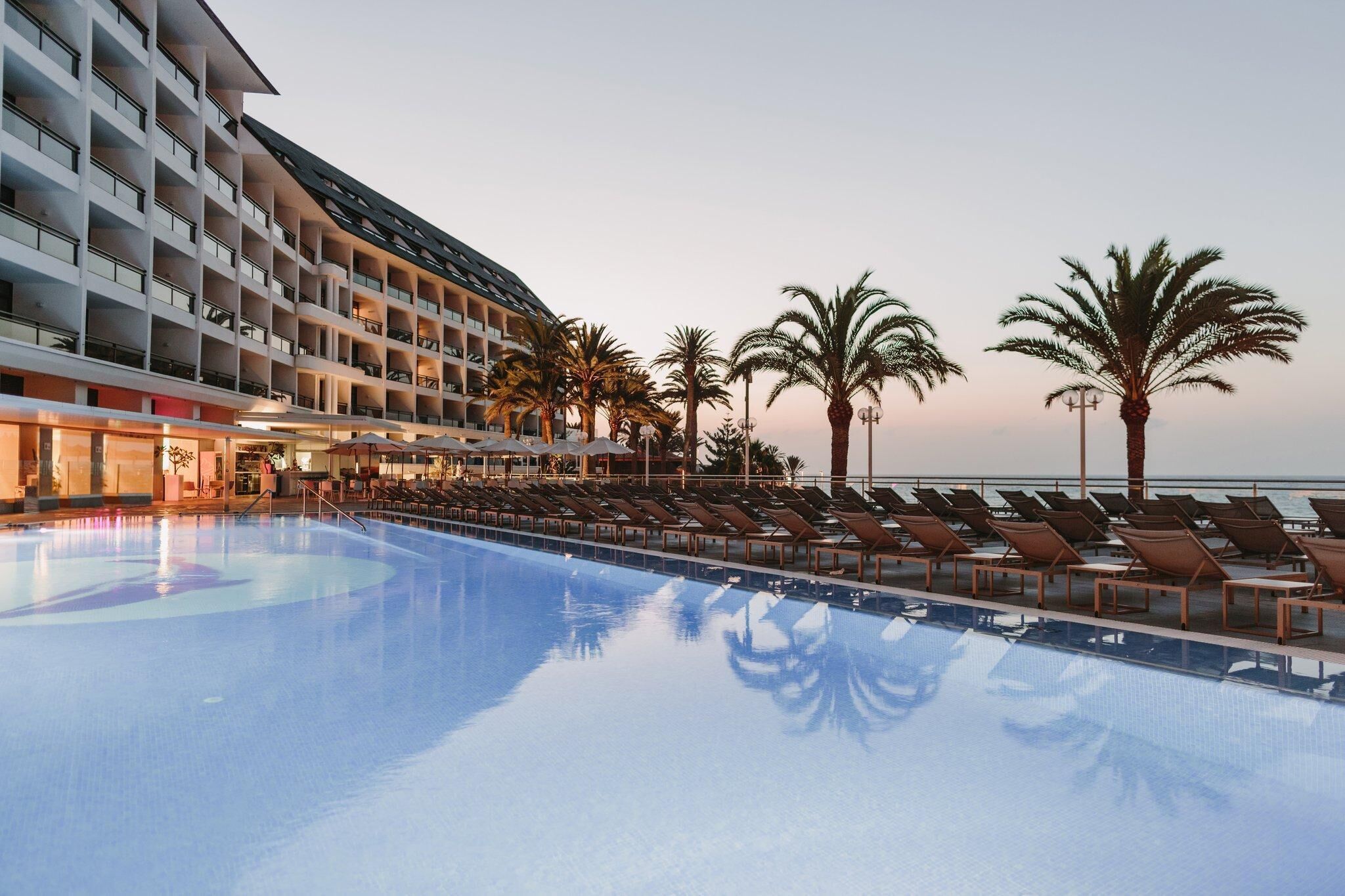 Un hotel con piscina, tumbonas y palmeras.