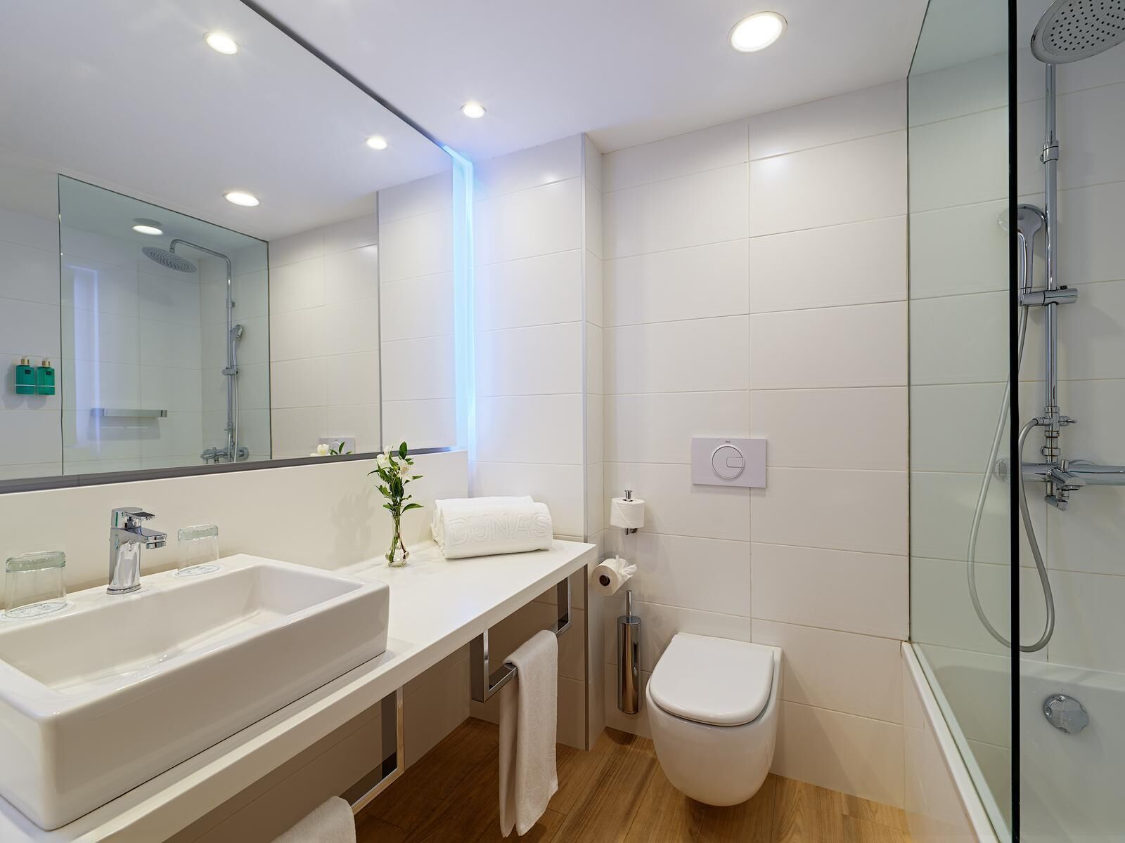 Un baño moderno con un espejo grande, dos lavamanos, un inodoro y una ducha con mampara de vidrio.
