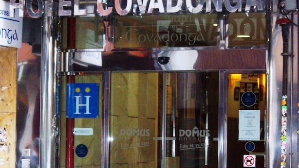 The entrance to Hotel Covadonga with a glass door, a blue sign with a white 'H', and two potted plants on the sidewalk. - City Express Covadonga (Oviedo)
