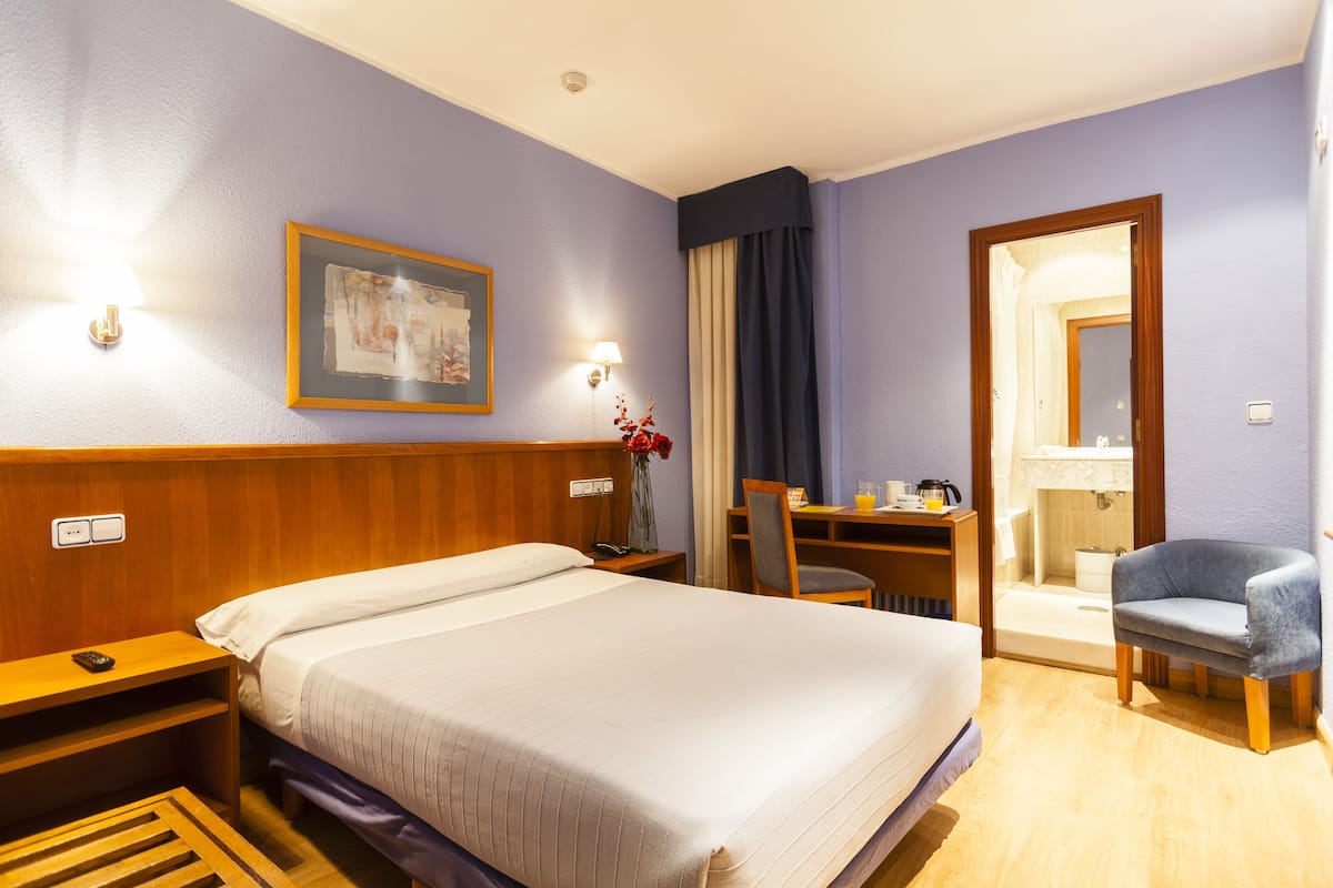 Een hotelkamer met een groot bed, een bureau met stoel, een spiegel en een badkamer die door een open deur zichtbaar is.