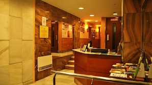 A hotel reception area with a marble wall, a reception desk, and a staircase leading to an upper floor. - City Express Covadonga (Oviedo)