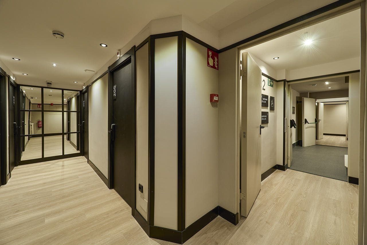 Un pasillo de hotel con un muro espejado, un detector de incendios y una puerta marcada con el número 2.