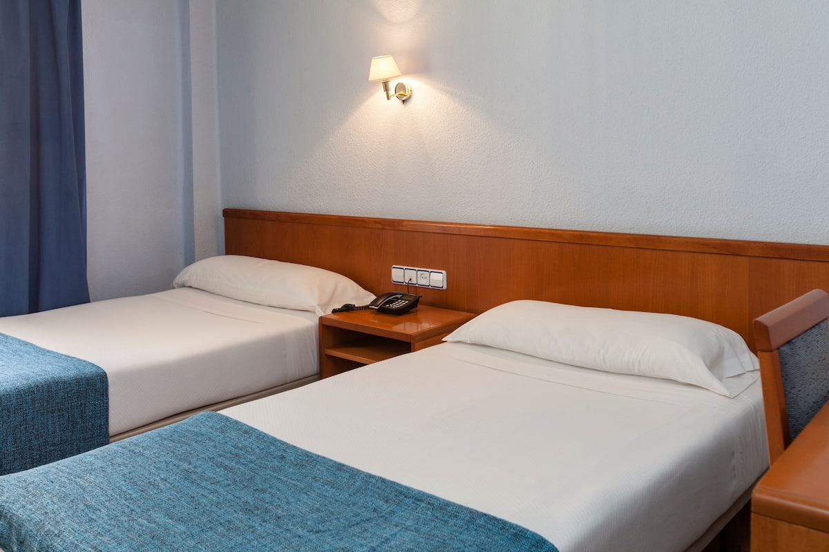 Een hotelkamer met twee enkele bedden, een houten hoofdbord, een nachtkastje met een telefoon en een wandlamp.