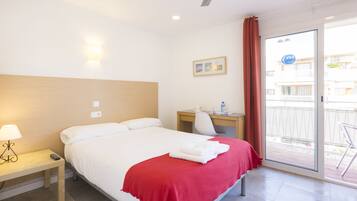 Habitación de hotel con cama, escritorio, silla, mesita de noche y puerta corrediza de vidrio al exterior.