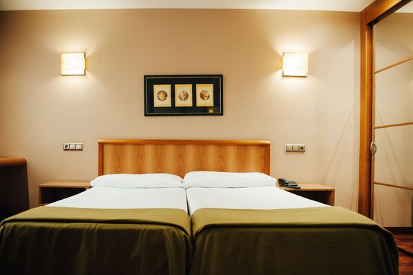 A hotel room with two beds, a wooden headboard, bedside tables with lamps, and a framed picture on the wall. - Hotel Carreño (Oviedo)