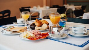 Disposição de café da manhã com croissants, presunto, queijo e uma bebida de frutas sobre uma mesa.