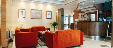 A lobby with red sofas, a reception desk, framed artwork on the walls, and a potted plant.