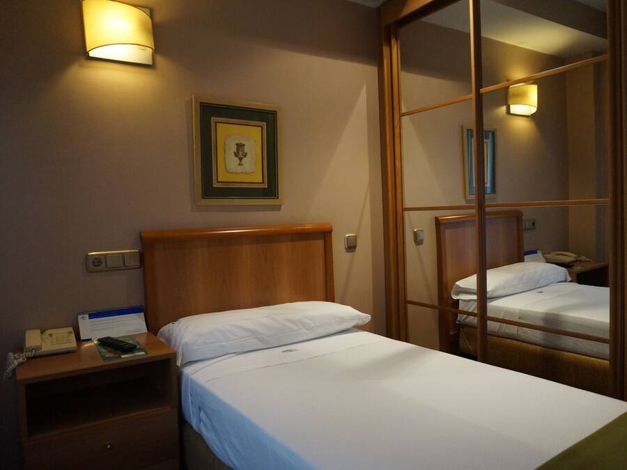Une chambre d’hôtel avec deux lits simples, une tête de lit en bois, des tables de chevet avec des lampes, un tableau encadré au mur et un miroir qui reflète la pièce.