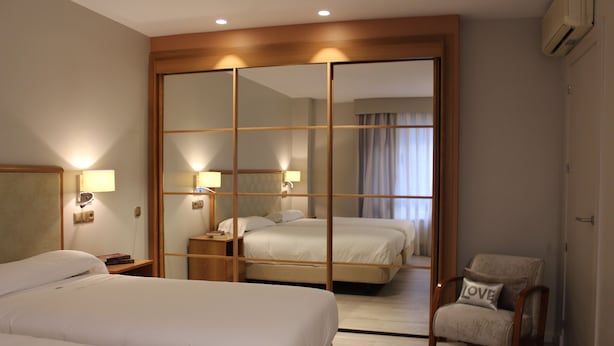 Quarto de hotel com duas camas, um espelho, uma cadeira e um guarda-roupa.