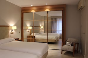 Una habitación de hotel con dos camas, un espejo, una silla y un armario.