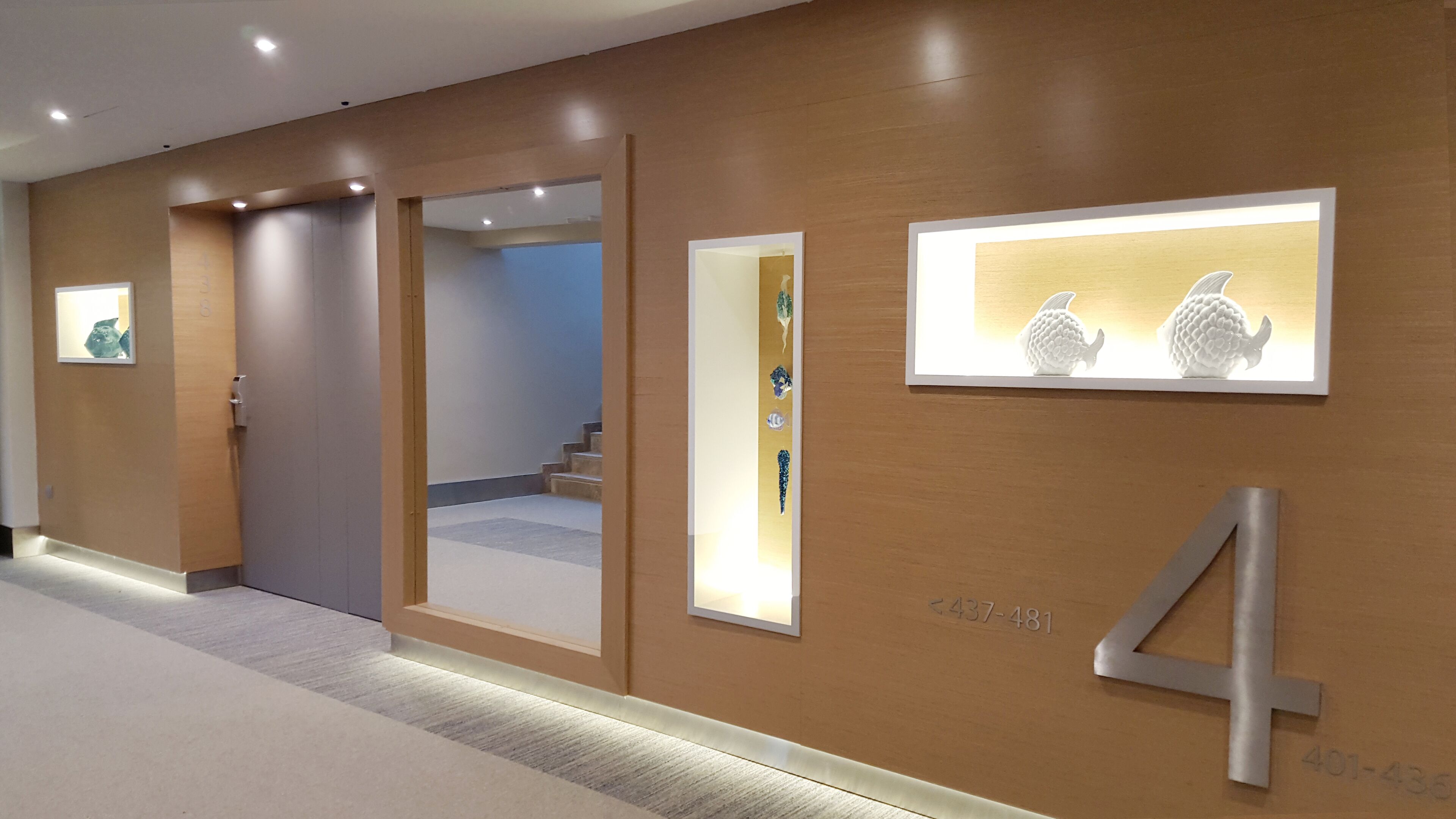A hallway with wooden walls, numbered doors, and illuminated wall art.