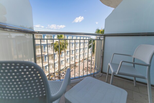 A balcony with white chairs and a table, overlooking a building with multiple balconies and palm trees.
