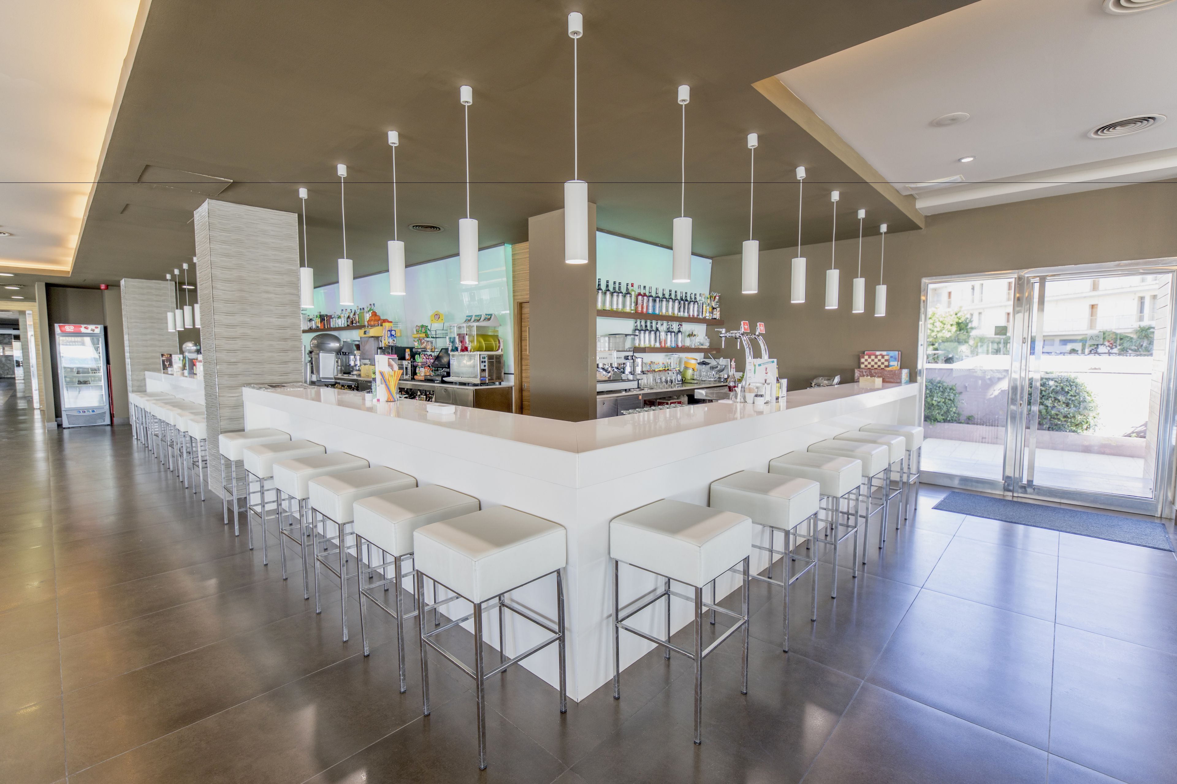 A modern bar area with white bar stools, a central counter, and pendant lighting.