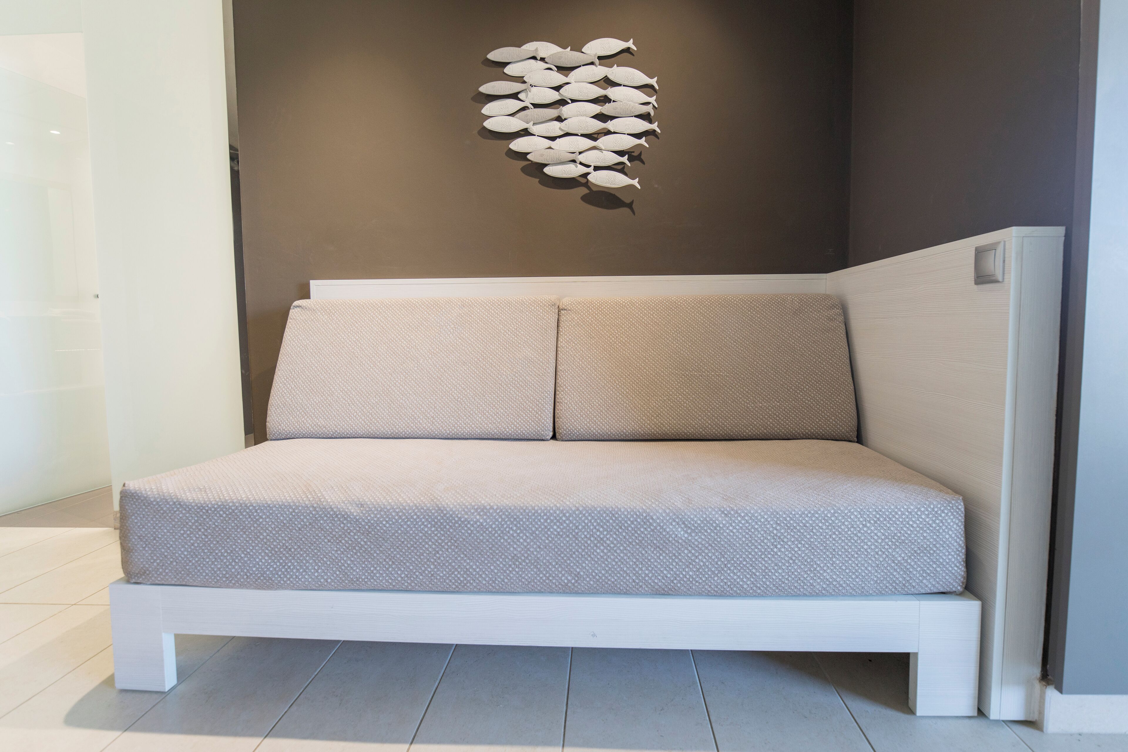 A modern, minimalist room with a white sofa against a dark wall, featuring a unique wall art piece.
