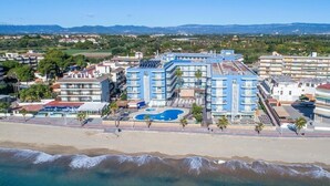 Un hotel frente al mar con varios pisos, piscina y vistas a la playa.