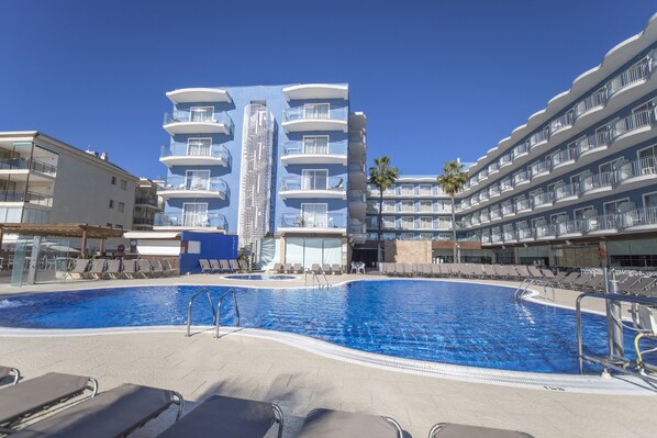 Un hotel con piscina, varios balcones y una palmera.