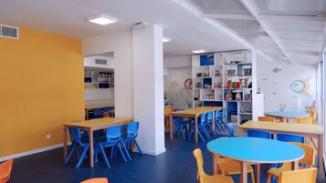 Un cuarto de juegos para niños con mesas y sillas, una estantería y un mural en la pared.