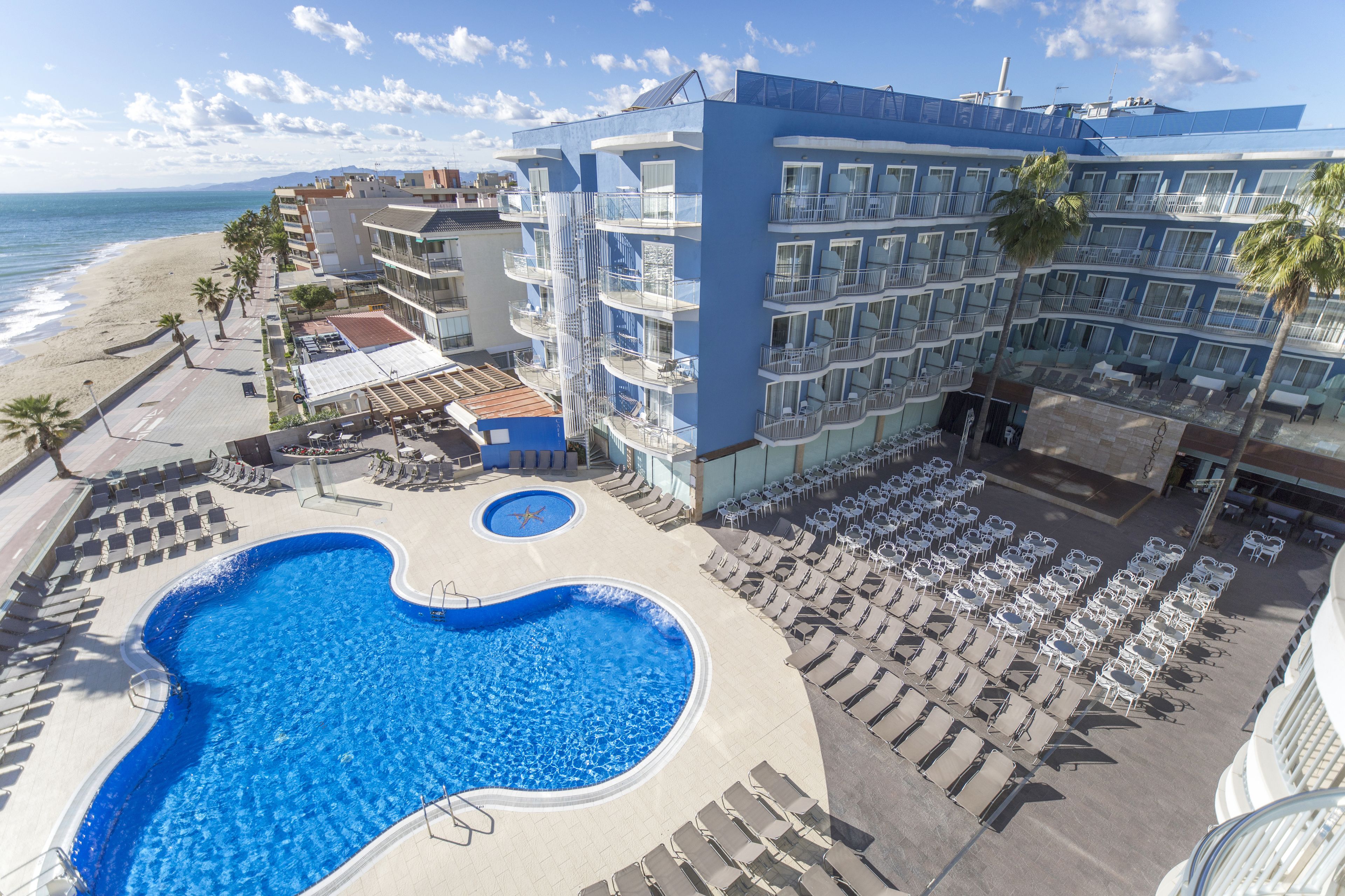 A hotel with a pool, sun loungers, and a view of the beach.