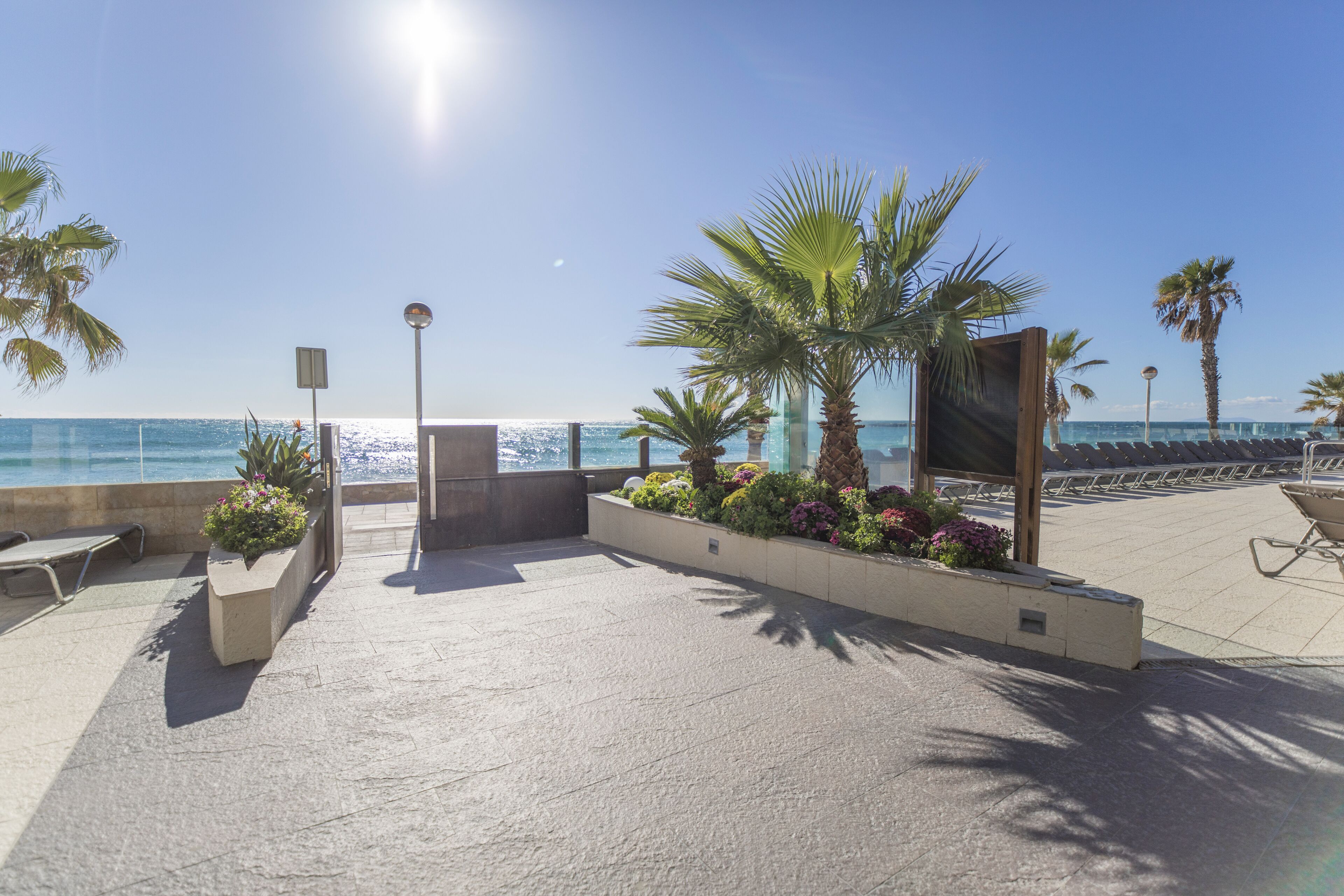 Un espace extérieur ensoleillé avec vue sur la mer, comprenant un coin salon agrémenté de jardinières et d’une structure en bois.